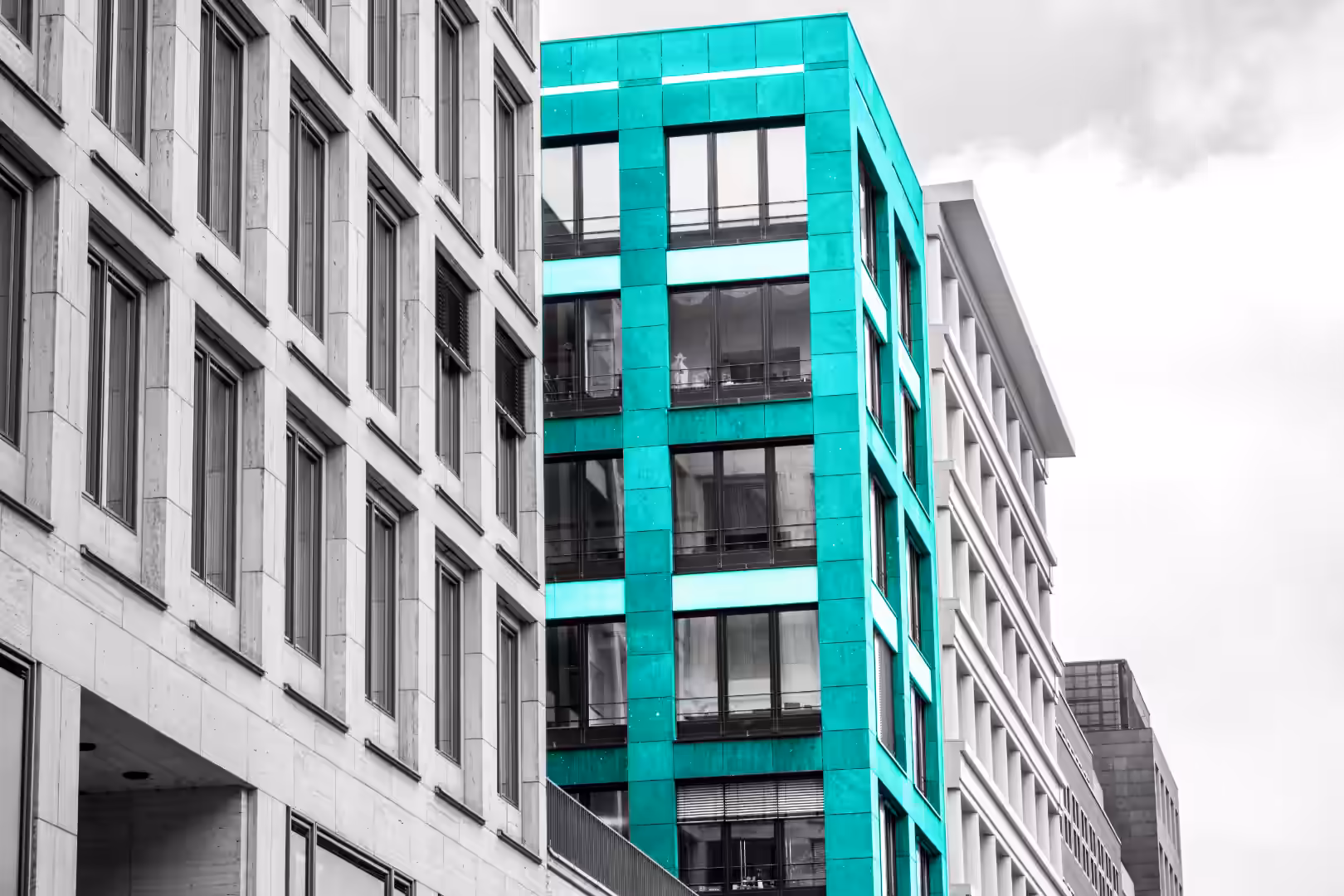Monochrome perspective of a modern corporate business district showing sleek office buildings in a row, with one complete central building facade selectively highlighted in bright teal.